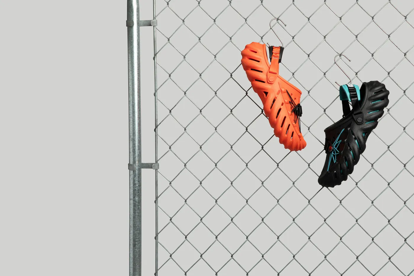 Two Crocs—orange and black—hanging from a chainlink fence. Urban-inspired display highlighting Crocs’ versatility and style.